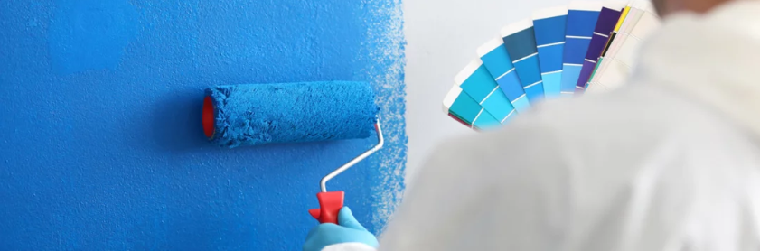 A painter painting a wall blue next to a section of blue paint chips.